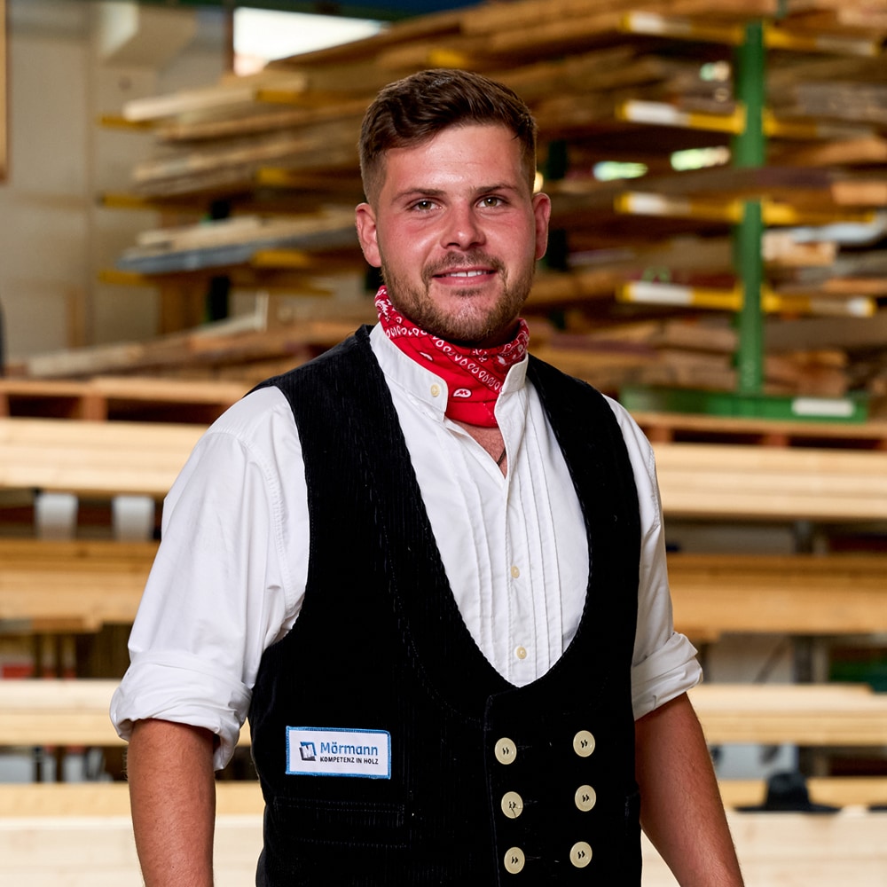 David Hörth in Zimmermannskluft mit rotem Halstuch vor dem Holzlager